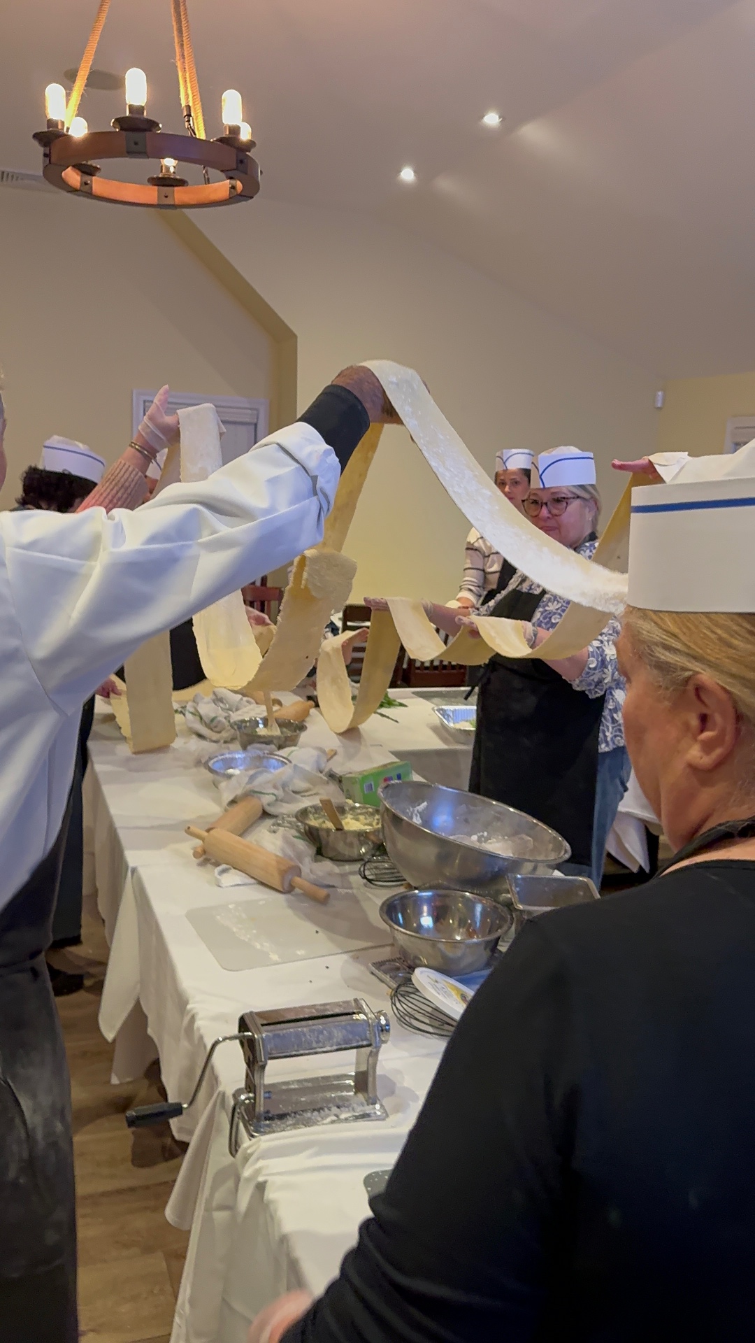 Chef stretching a long ribbon of fresh pasta dough above the table
